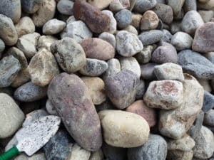 Assortment of smooth, multi-colored landscaping rocks piled together with a gardening trowel.
